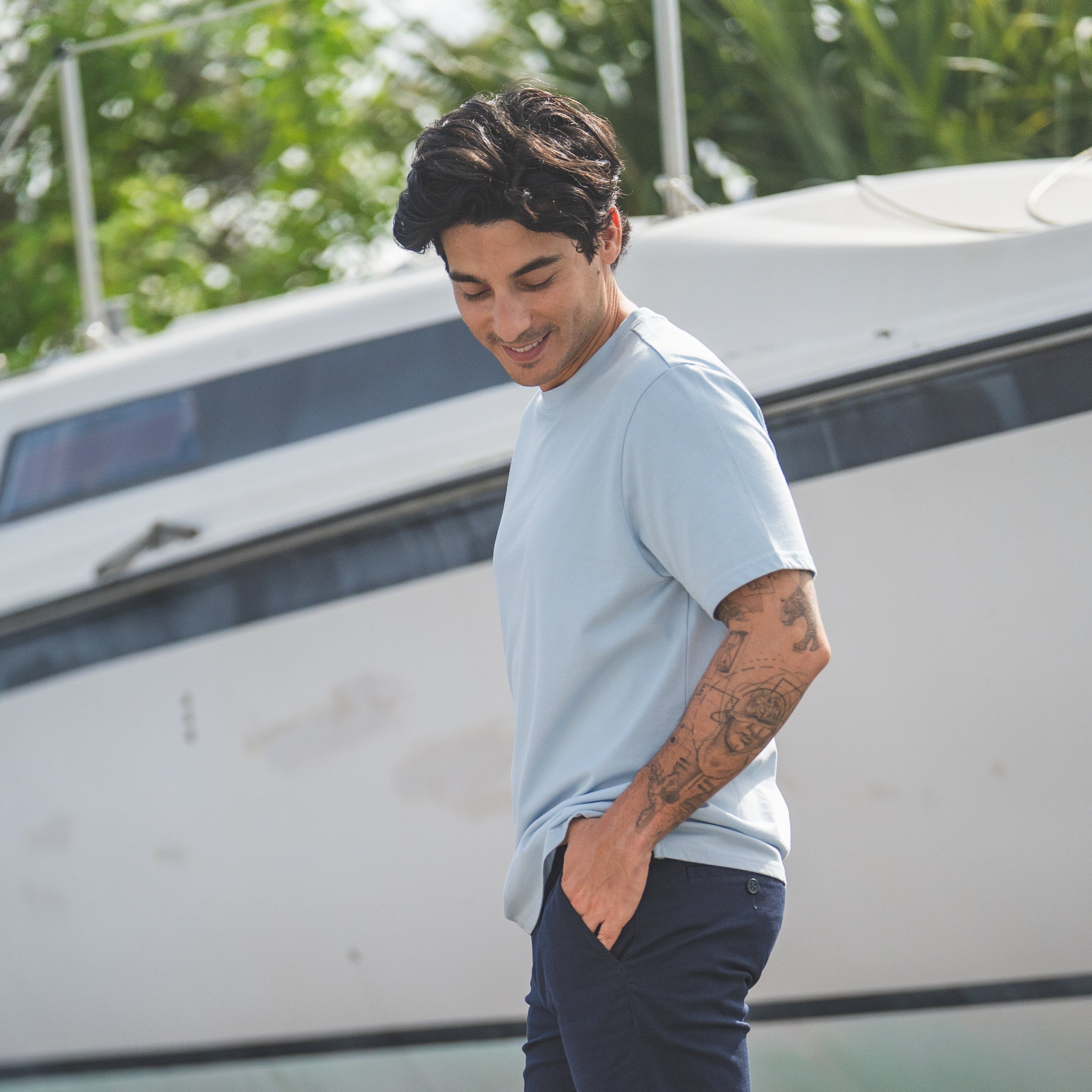 Man standing in front of a boat wearing a light gray t-shirt, dark blue pants, and white sneakers.
